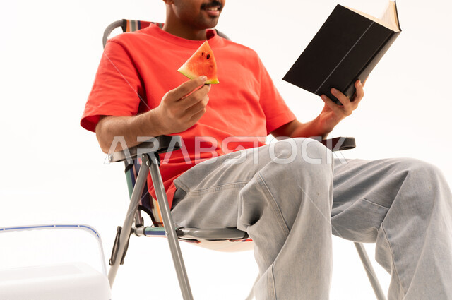 Man Reading Book and Eating Watermelon in Studio