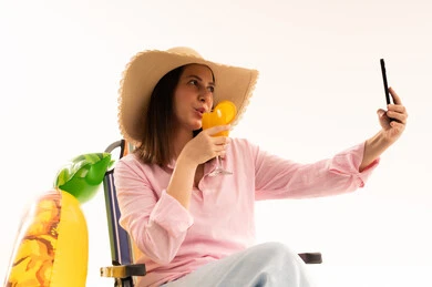 امرأة على كرسي الشاطئ تلتقط سيلفي مع عصير