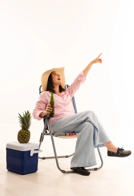 امرأة تجلس على كرسي شاطئ وتشير للأعلى بخلفية بيضاء