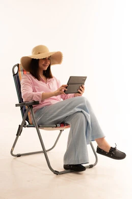 امرأة عربية تستخدم جهاز لوحي على كرسي شاطئ