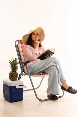 امرأة على كرسي شاطئ تقرأ كتاباً مع أناناس