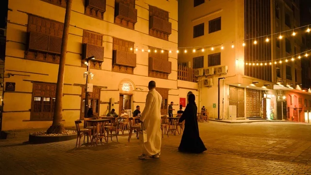 رجل وامرأة سعوديين يسيران في ساحة تقليدية ليلاً