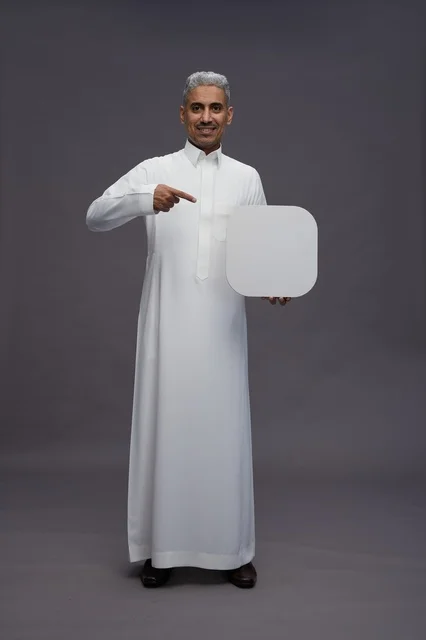 رجل سعودي بالثوب يشير إلى لوحة فارغة في استوديو رجل سعودي بالثوب يشير إلى لوحة فارغة في استوديو