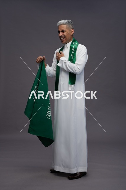 رجل سعودي بالثوب يحمل العلم الوطني في الاستوديو