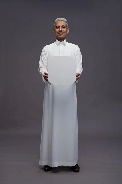 رجل سعودي يحمل لوحة بيضاء فارغة في الاستوديو