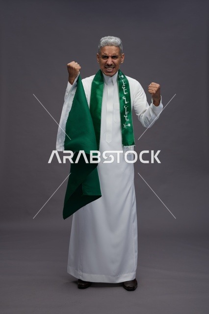 رجل سعودي مسن يحتفل بالعلم على خلفية رمادية