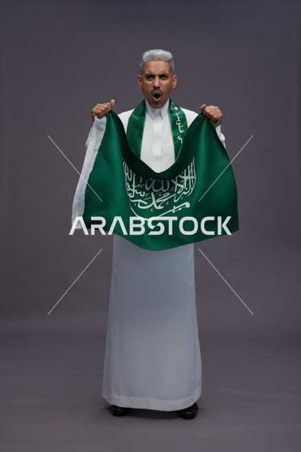 رجل سعودي يحمل العلم الوطني ويحتفل بخلفية رمادية