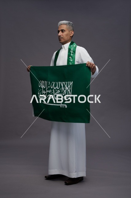 رجل سعودي بالثوب التقليدي يحمل علم المملكة