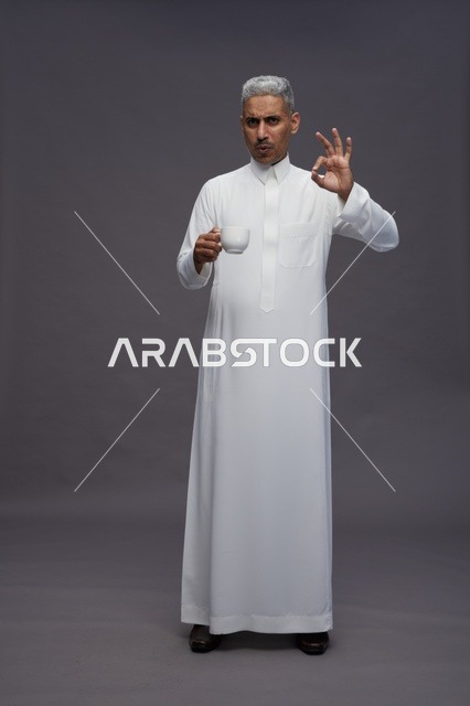 رجل سعودي بالثوب الأبيض يحمل فنجان قهوة