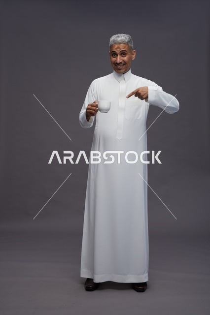 رجل سعودي بالثوب الأبيض يشير إلى فنجان قهوة