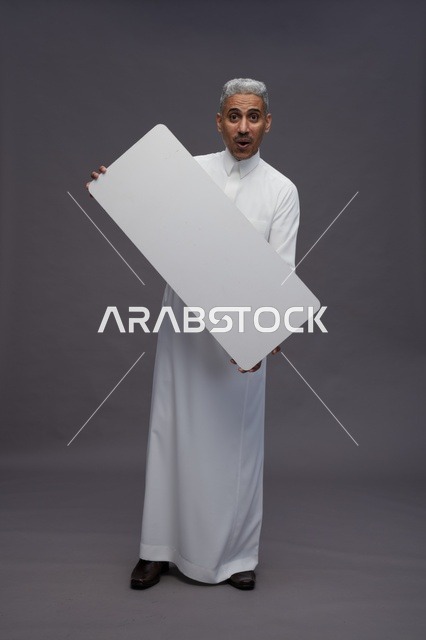 رجل سعودي يحمل لوحة بيضاء فارغة خلفية رمادية