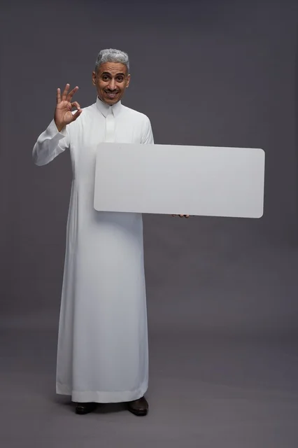 رجل سعودي بالثوب يحمل لوحة بيضاء وإشارة الموافقة