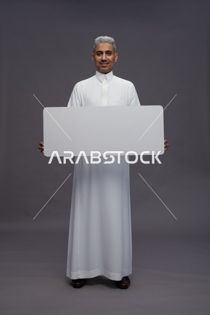 رجل سعودي يحمل لوحة بيضاء فارغة بخلفية رمادية