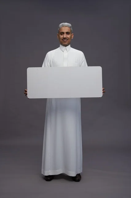 رجل سعودي يحمل لوحة بيضاء فارغة بخلفية رمادية