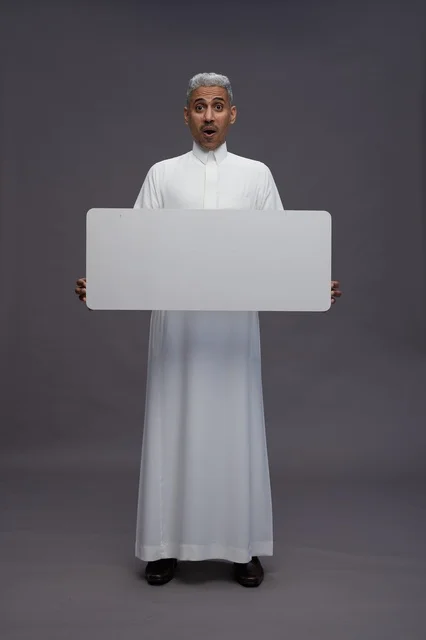 رجل سعودي مندهش يمسك لوحة بيضاء فارغة في الاستوديو
