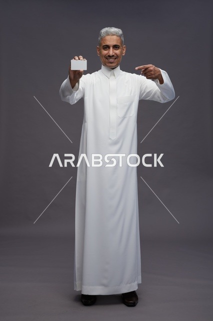 رجل سعودي بالثوب يحمل بطاقة بيضاء فارغة خلفية رمادية