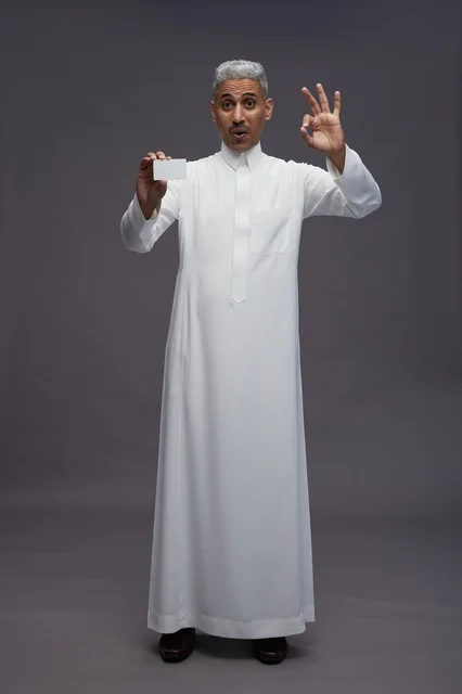 رجل سعودي بالثوب يحمل بطاقة بيضاء مع إيماءة موافق