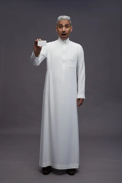 رجل عربي متفاجئ يرتدي الثوب ويمسك بطاقة عمل بيضاء