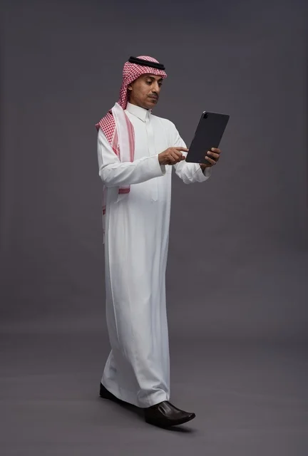 رجل سعودي يستخدم جهاز لوحي بخلفية استوديو رمادية