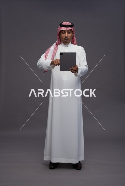رجل سعودي مندهش مع جهاز لوحي بخلفية رمادية