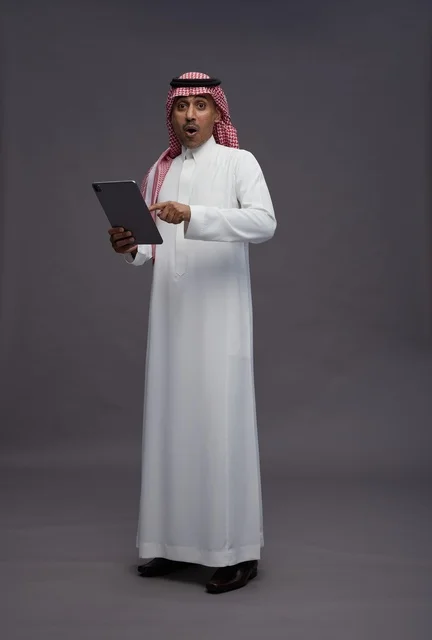 رجل سعودي متفاجئ يحمل جهاز لوحي في الاستوديو