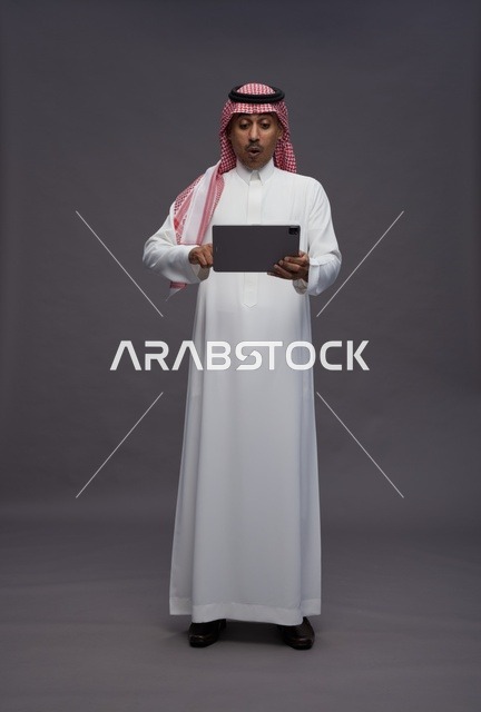 Surprised Saudi Man Using Tablet on Grey Background