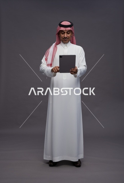 رجل سعودي بالثوب التقليدي يستخدم جهاز لوحي رقمي