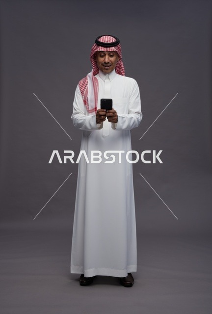 رجل سعودي يحمل هاتف ذكي في استوديو خلفية رمادية