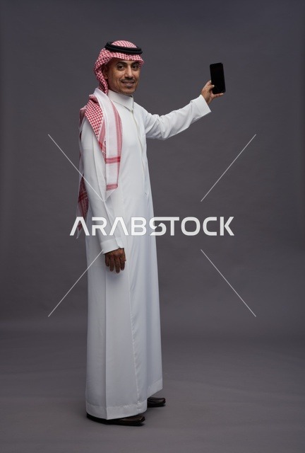 رجل سعودي بالزي التقليدي يحمل هاتف جوال