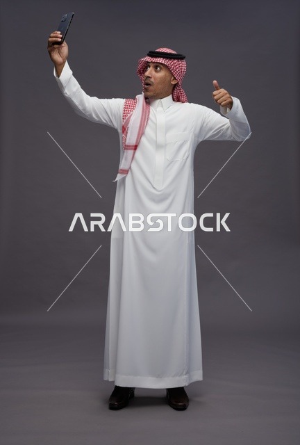 رجل سعودي بالثوب يلتقط سيلفي مع إشارة الإبهام