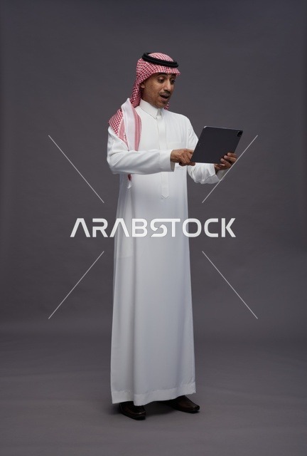 رجل سعودي يستخدم جهاز لوحي بتعبيرات وجه متفاجئة