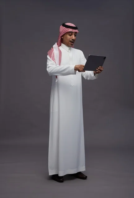 رجل سعودي يستخدم جهاز لوحي بتعبيرات وجه متفاجئة