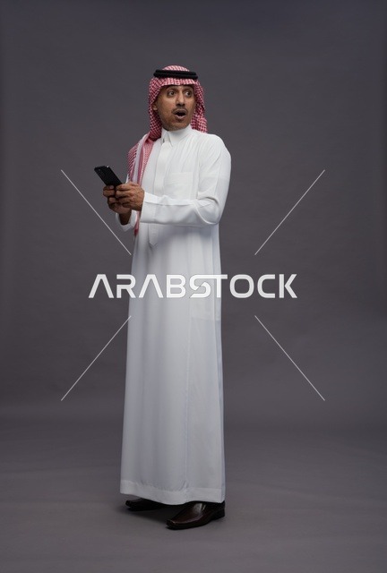 رجل سعودي مندهش يحمل هاتف ذكي خلفية رمادية