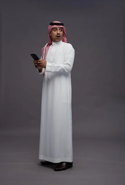 رجل سعودي مندهش يحمل هاتف ذكي خلفية رمادية