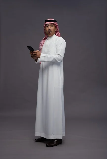 Surprised Saudi Man Holding Smartphone in Studio