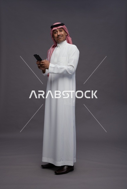 رجل سعودي يحمل هاتف ذكي بخلفية رمادية