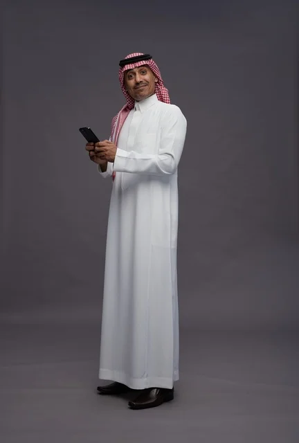 رجل سعودي يحمل هاتف ذكي بخلفية رمادية