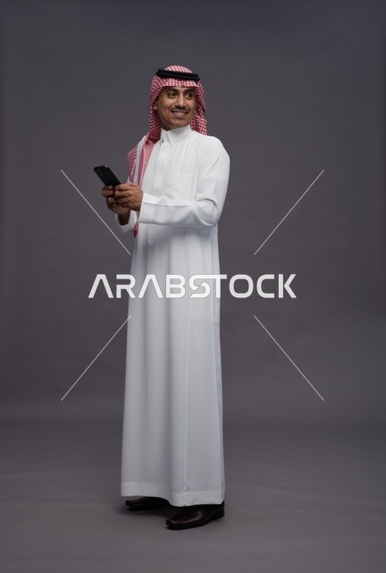 رجل سعودي مع هاتف ذكي بخلفية رمادية
