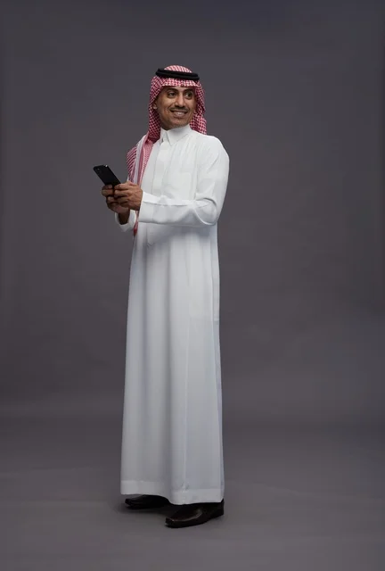 رجل سعودي مع هاتف ذكي بخلفية رمادية