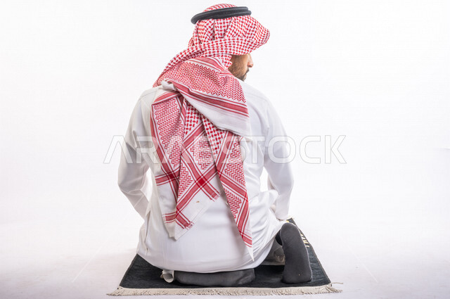 بورتريه من الخلف لرجل عربي سعودي خليجي يرتدي الثوب الأبيض والشماغ يؤدي الصلاه, الجلوس على سجادة الصلاه, الإكثار من ذكر الله تعالى, الإستغفار والدعاء, الإجتهاد في العباده, التقرب الى الله تعالى في شهر رمضان المبارك, جمعه مباركه, إسلاميات وعبادات