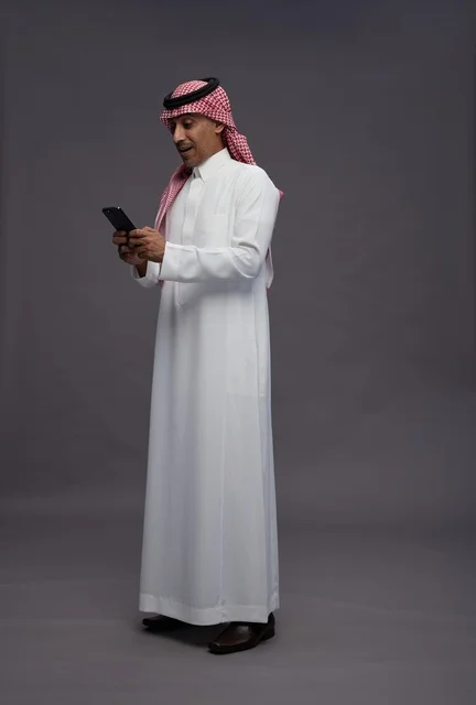 رجل سعودي ينظر إلى هاتفه الذكي بخلفية رمادية