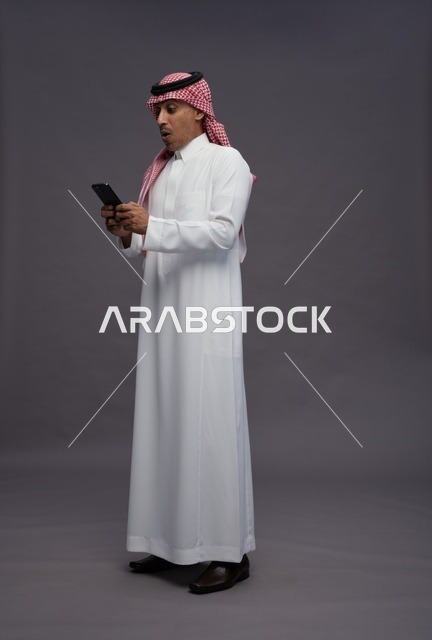 رجل سعودي متفاجئ يستخدم الهاتف الذكي بخلفية رمادية