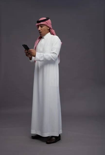 رجل سعودي متفاجئ يستخدم الهاتف الذكي بخلفية رمادية