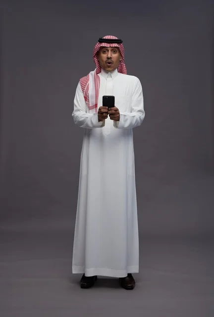 Shocked Saudi Man Holding Smartphone on Grey Background