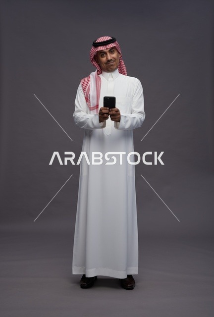 رجل سعودي بالزي التقليدي يمسك هاتف ذكي في الاستوديو