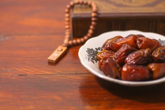 تمر رمضان وسبحة خشبية على طاولة داكنة