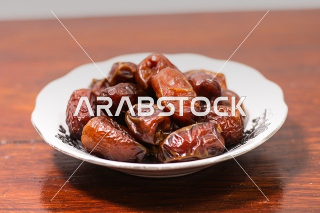 Dried dates in a white ceramic bowl on a warm wooden table for Ramadan breakfast.