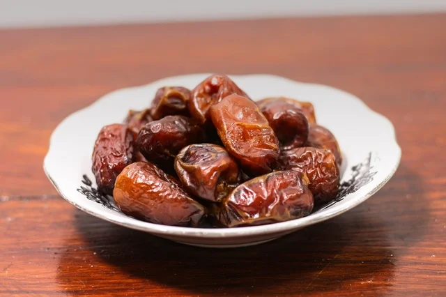 Dried dates in a white ceramic bowl on a warm wooden table for Ramadan breakfast. Dried dates in a white ceramic bowl on a warm wooden table for Ramadan breakfast.