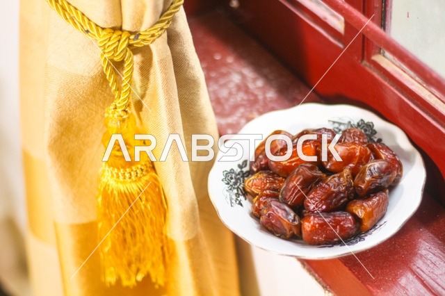 طبق تمر طازج على حافة النافذة مع ستارة ذهبية فى اجواء رمضانية