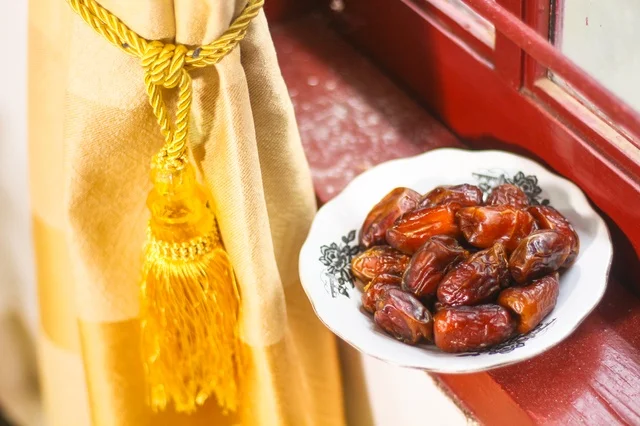 طبق تمر طازج على حافة النافذة مع ستارة ذهبية فى اجواء رمضانية